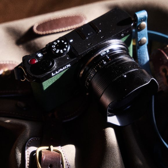 A black Lumix camera with a lens sits on a tan bag with leather straps in dramatic light.