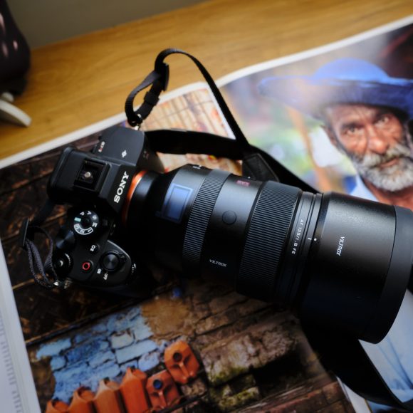 Camera with a large lens rests on an open magazine featuring a portrait of an elderly man in a blue hat.