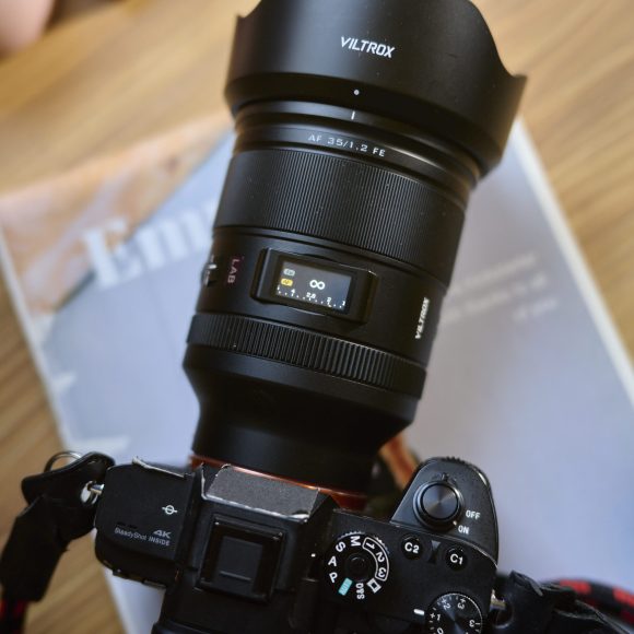 A Viltrox camera with a large lens sits on top of a magazine on a wooden table.