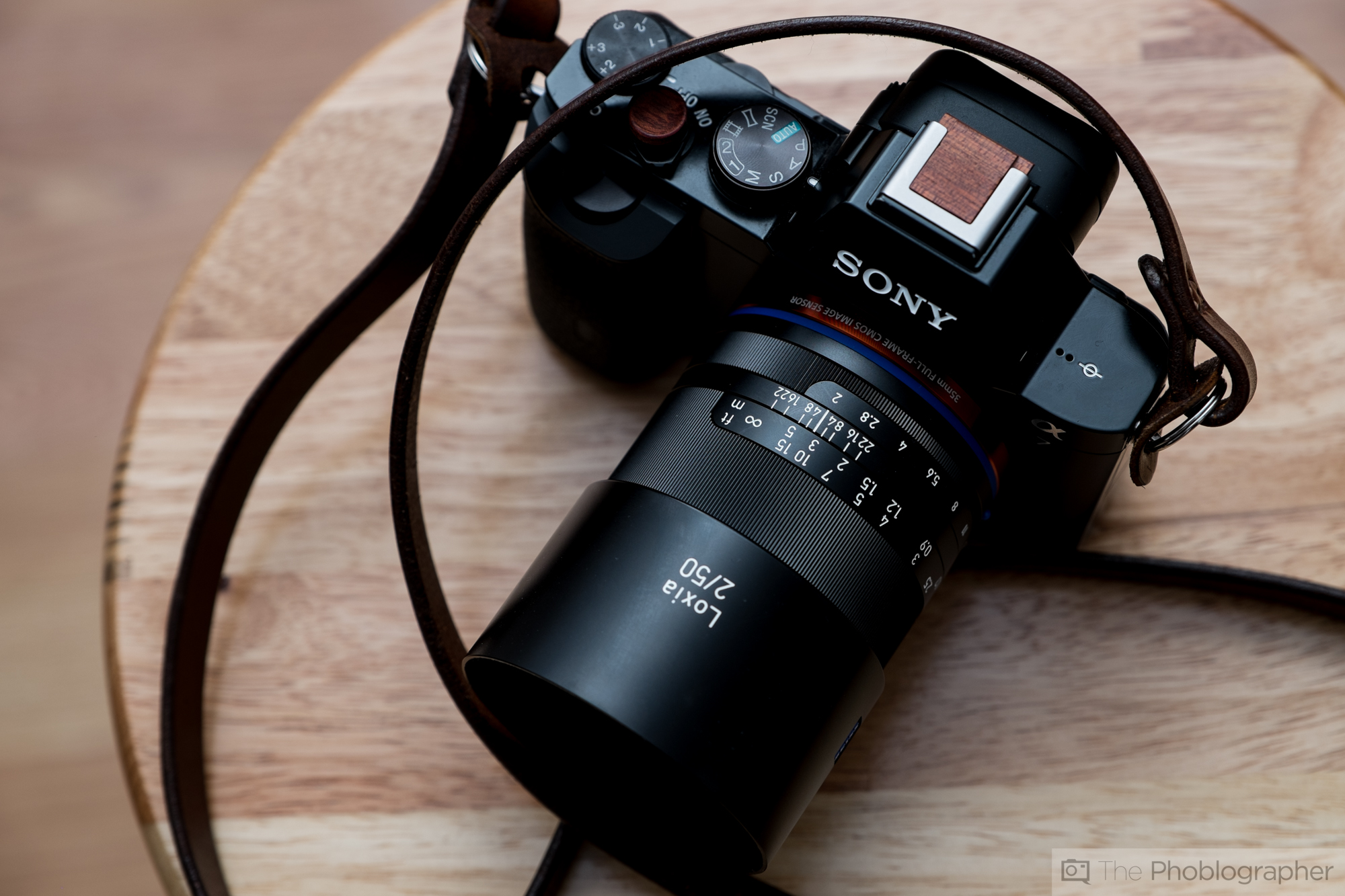 Sony camera with a Zeiss Loxia 2/50 lens and a brown strap resting on a wooden surface.