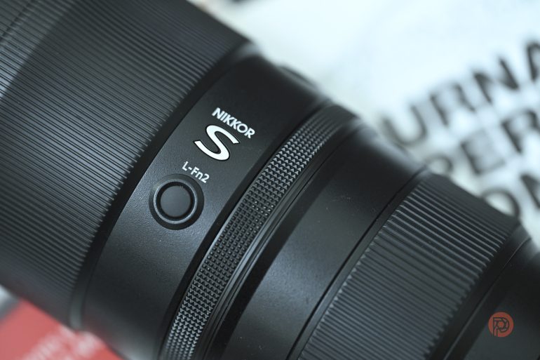 Close-up of a NIKKOR S camera lens with focus and function buttons visible.