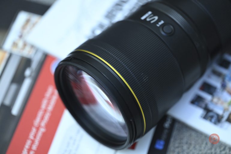Close-up of a camera lens placed on top of scattered papers and magazines.