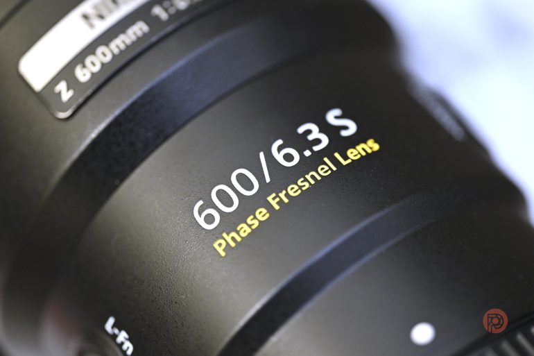 Close-up of a camera lens labeled 600/6.3 S Phase Fresnel Lens with yellow and white text on black surface.