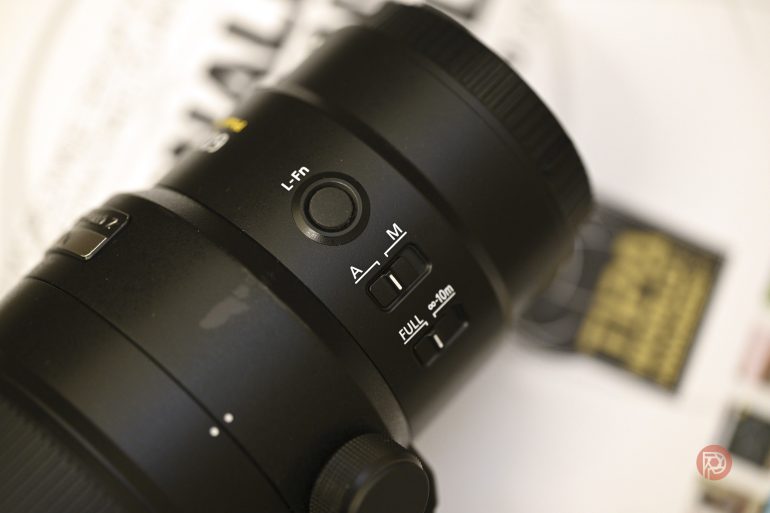 Close-up of camera lens showing buttons and switches for focus modes and custom settings.