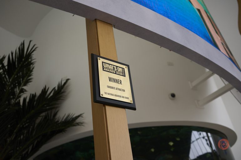 A gold Whats On Award Series Winner plaque is mounted on a wooden post inside a modern building.
