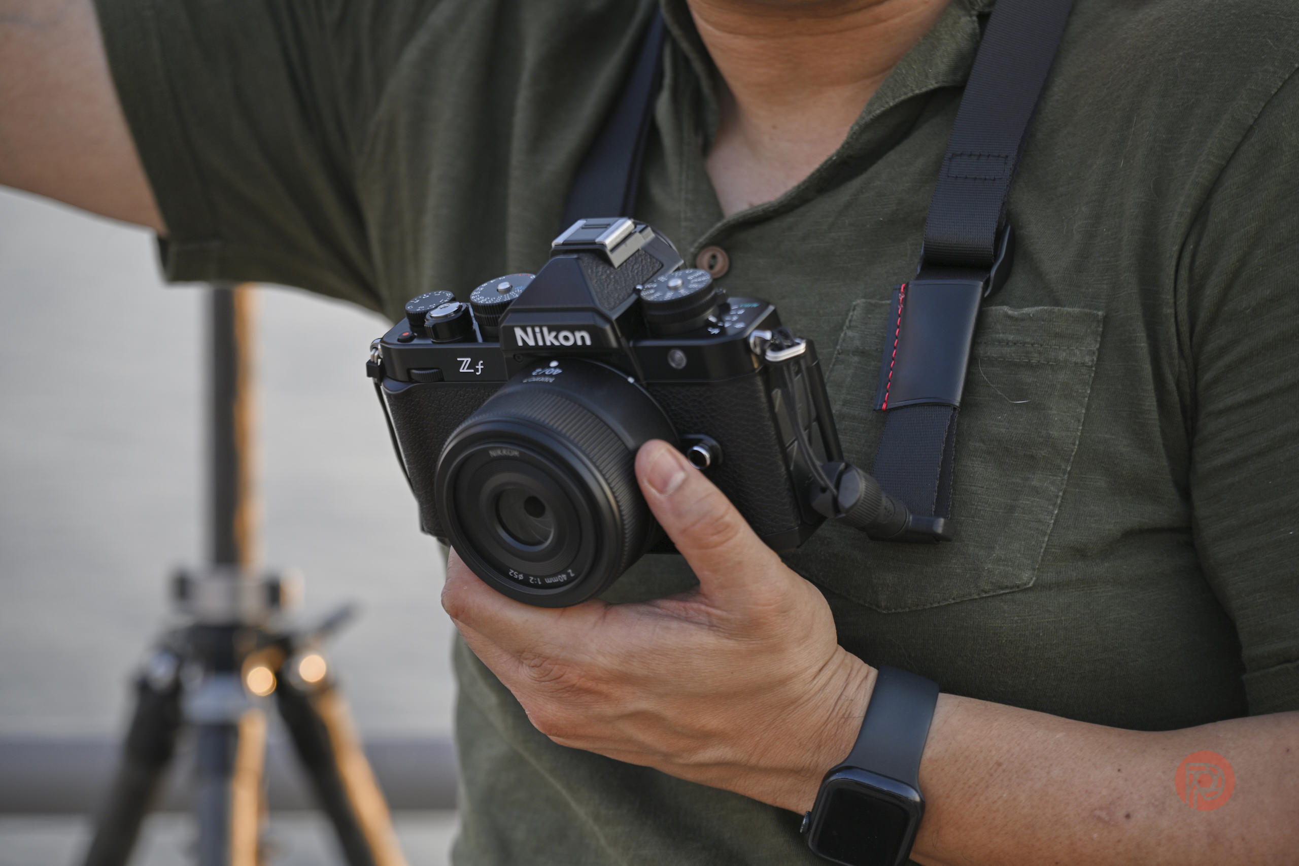 This Photographer Tried To Document an Entire Society. But Did it Work? Person holding a Nikon Zfc camera with a wide-angle lens, tripod blurred in the background.