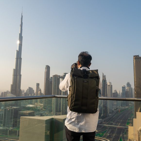 Person with backpack taking a photo of a city skyline with tall modern buildings and clear sky.