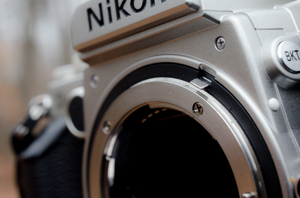 Close-up of a silver Nikon camera body with the lens removed, showing the lens mount.
