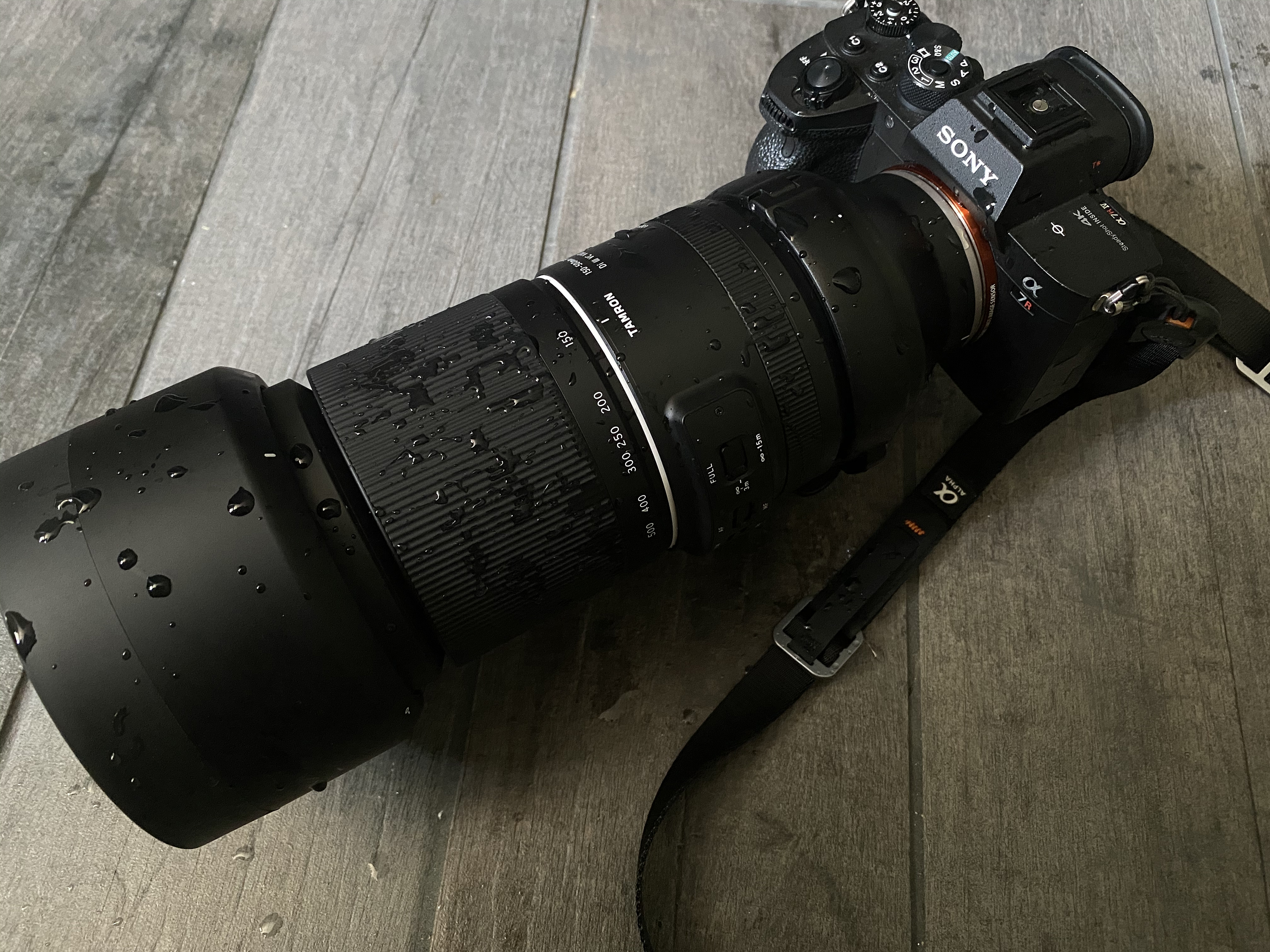 A Sony camera with a long, water-dropped zoom lens rests on a wooden surface.