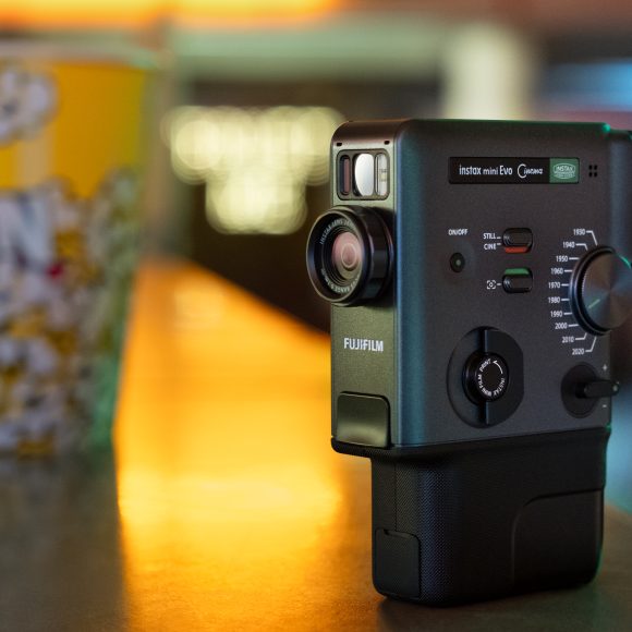A Fujifilm Instax Mini Evo camera on a counter next to a yellow popcorn tub in a softly lit room.