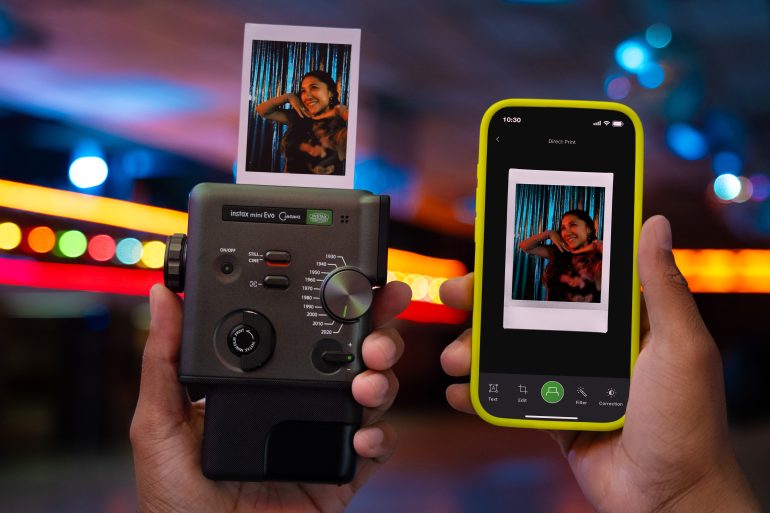 A hand holds a camera printing a photo, while another hand displays the same photo on a smartphone screen.