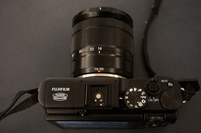 Top view of a Fujifilm digital camera with a 16-50mm lens on a dark surface.