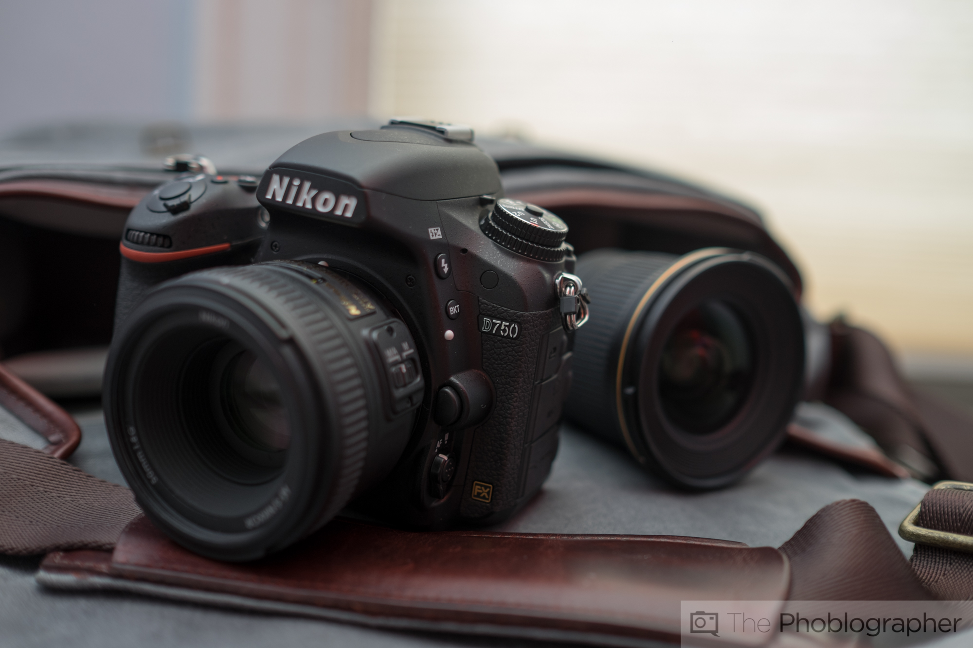 Nikon D750 camera with lens, accompanied by another lens, on a soft surface.