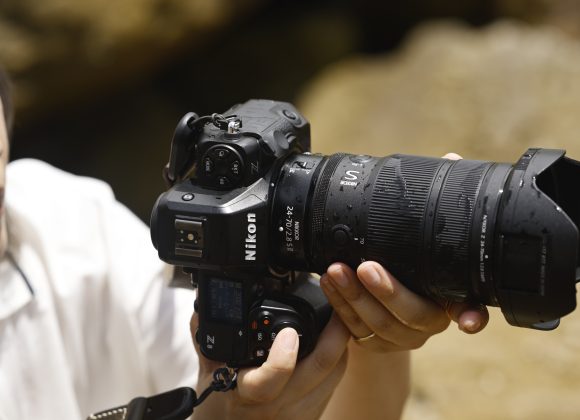 Person holding a Nikon Z camera with a large zoom lens attached, adjusting settings outdoors.