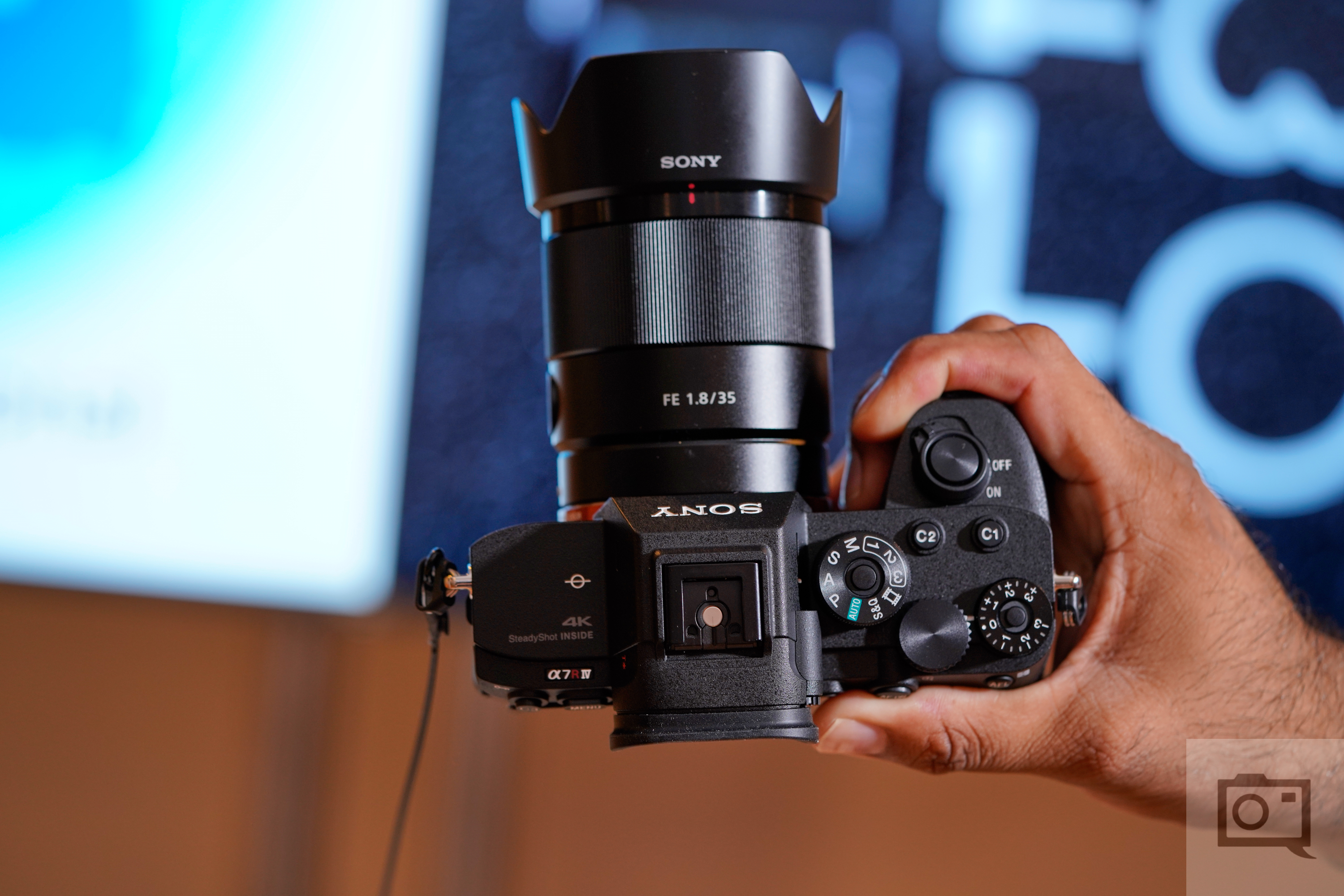 A hand holding a Sony Alpha 7 III camera with a FE 1.8/35 lens, viewed from above.