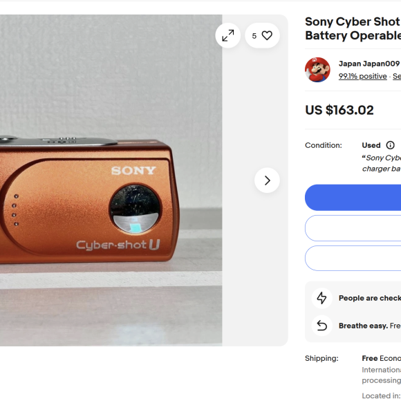 Orange Sony Cyber-shot DSC-U30 digital camera displayed on a white surface next to a wall.