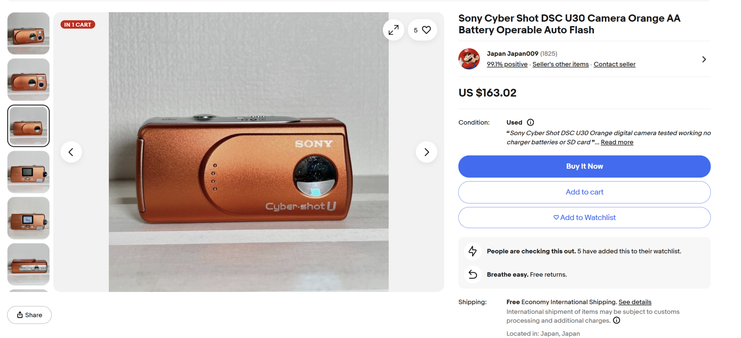 Orange Sony Cyber-shot DSC-U30 digital camera displayed on a white surface next to a wall.