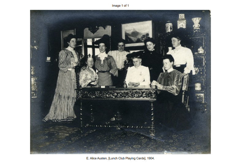 Seven women pose around a table with playing cards in a Victorian-era room, circa 1904.